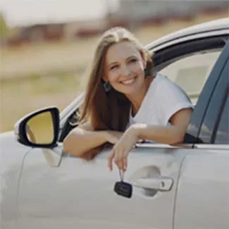 Smiling young driver leaning out of a car window holding her keys