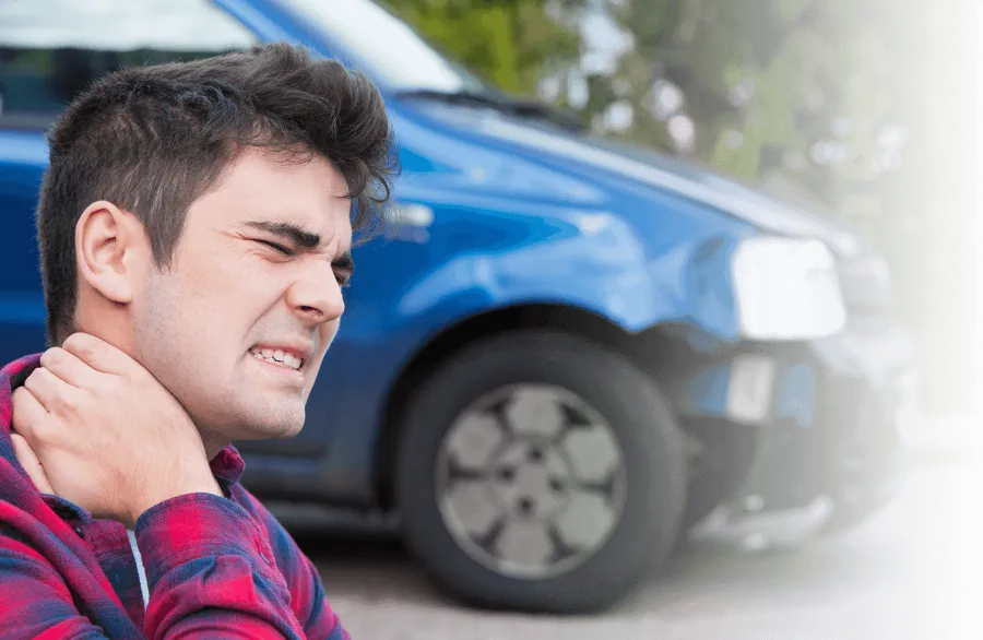 Man holding his neck in pain beside a damaged car after a collision