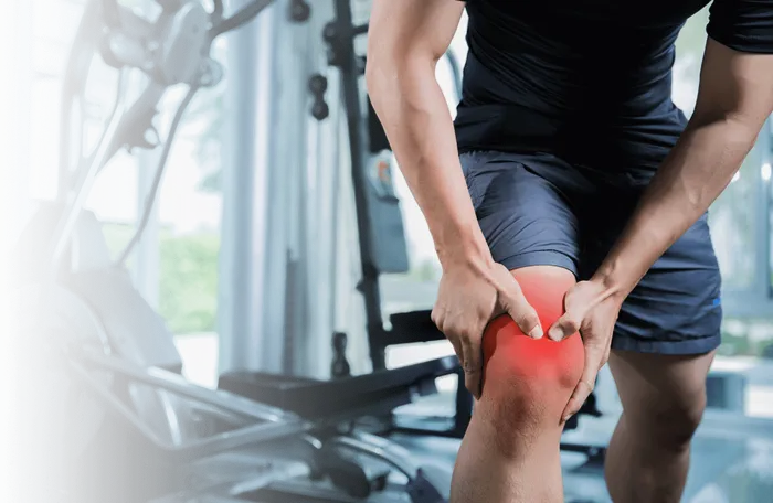 Athlete gripping an injured knee in a gym with rehabilitation equipment